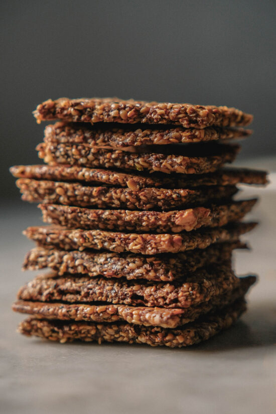 A side on image of high protein crackers in a stack on a white ceramic table against a dark backdrop
