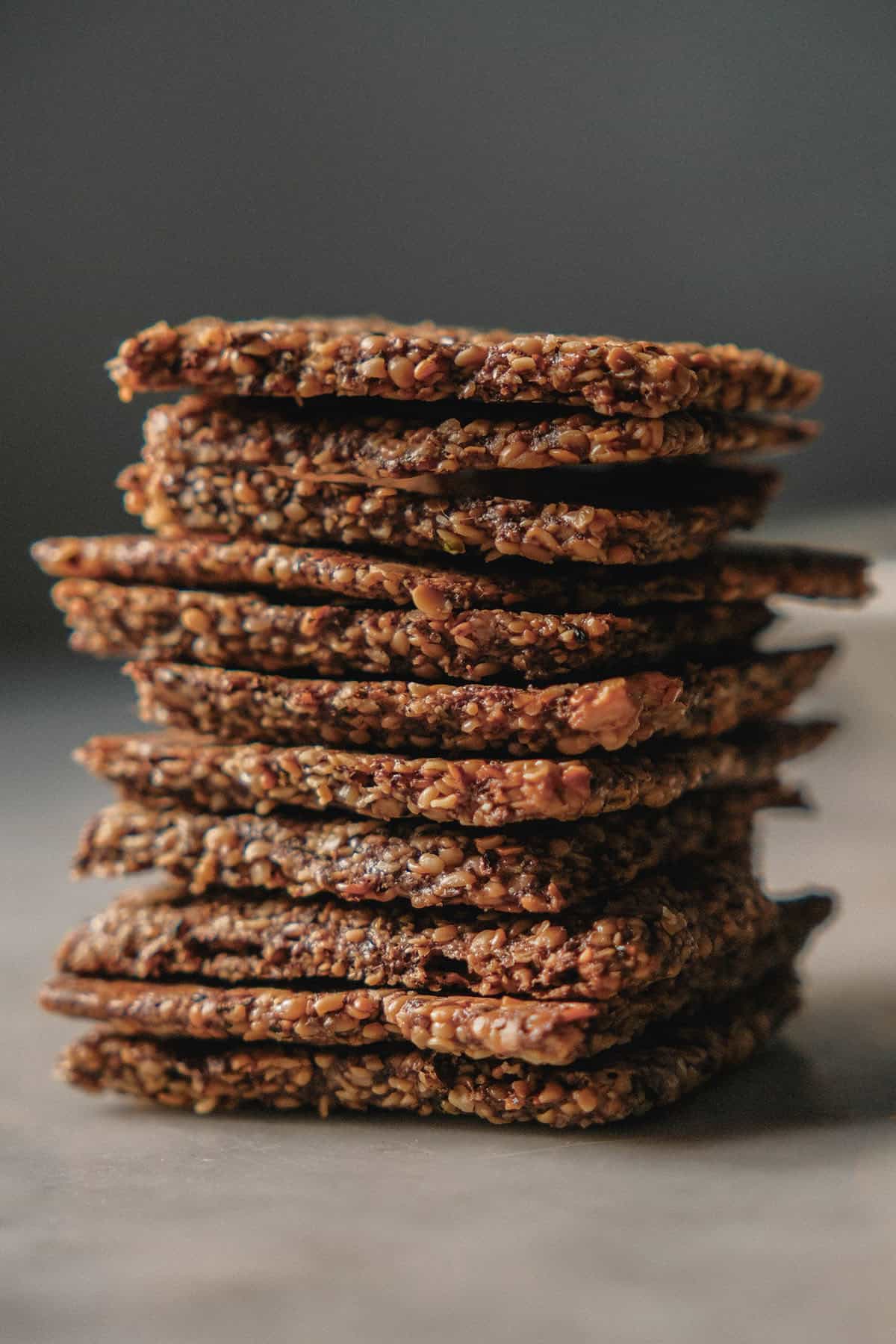 A side on image of high protein crackers in a stack on a white ceramic table against a dark backdrop