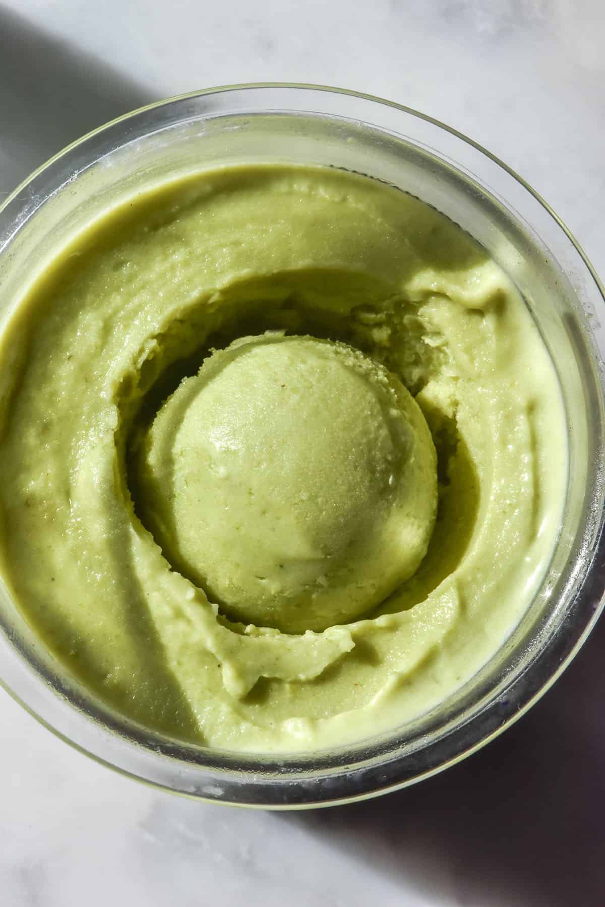 An aerial close up image of a tub of Ninja Creami pistachio ice cream on a white marble table