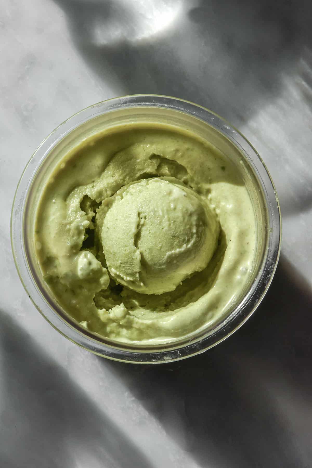 An aerial image of a tub of Ninja Creami vegan pistachio ice cream on a sunlit white marble table