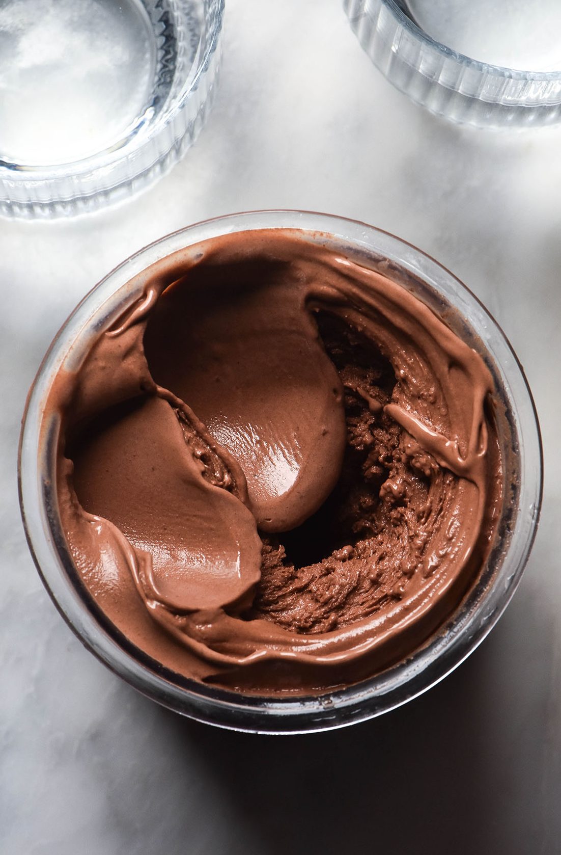 An aerial image of a tub of dark chocolate Ninja Creami ice cream atop a white marble table