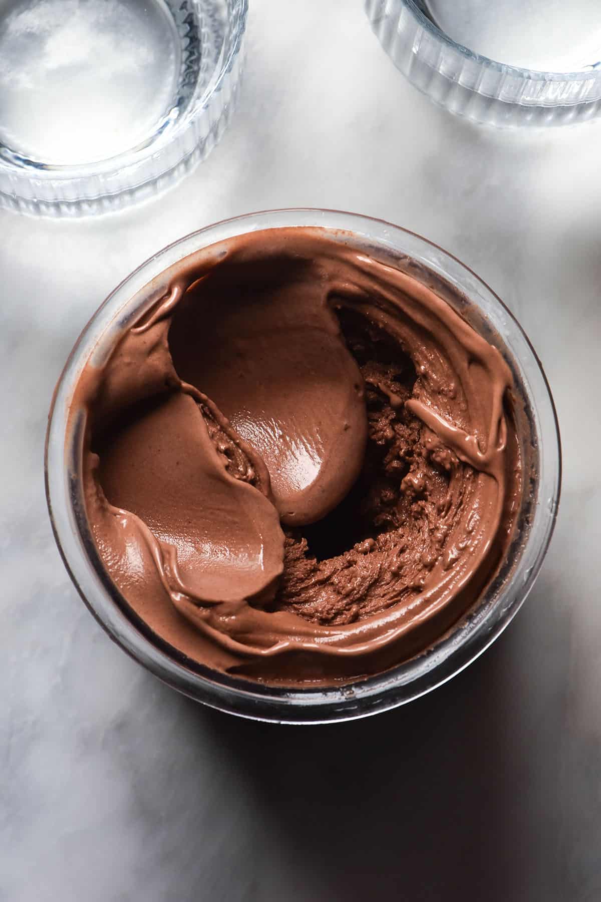 An aerial image of a tub of dark chocolate Ninja Creami ice cream atop a white marble table