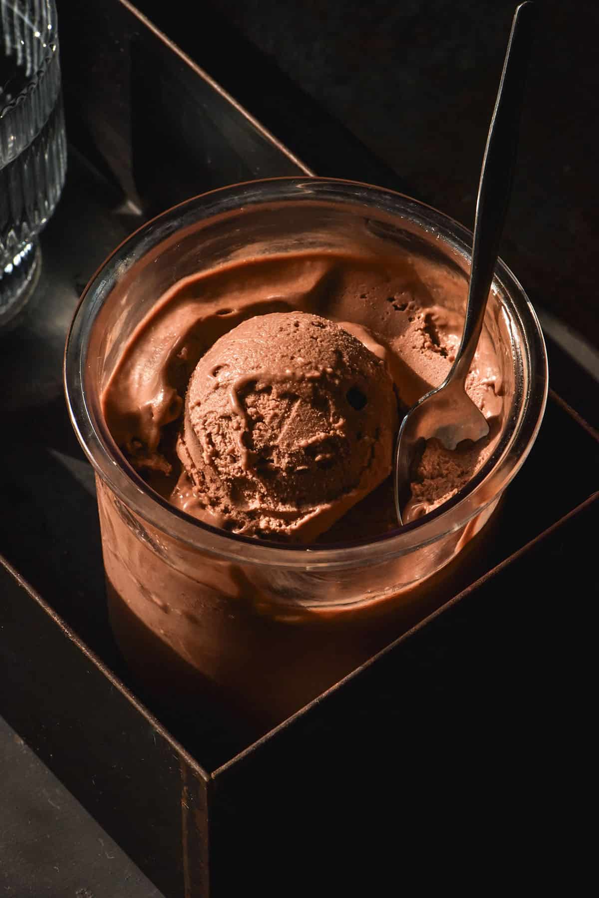 A moody side on image of a tub of vegan Nutella Ninja Creami ice cream on a black background in contrasting sunlight.