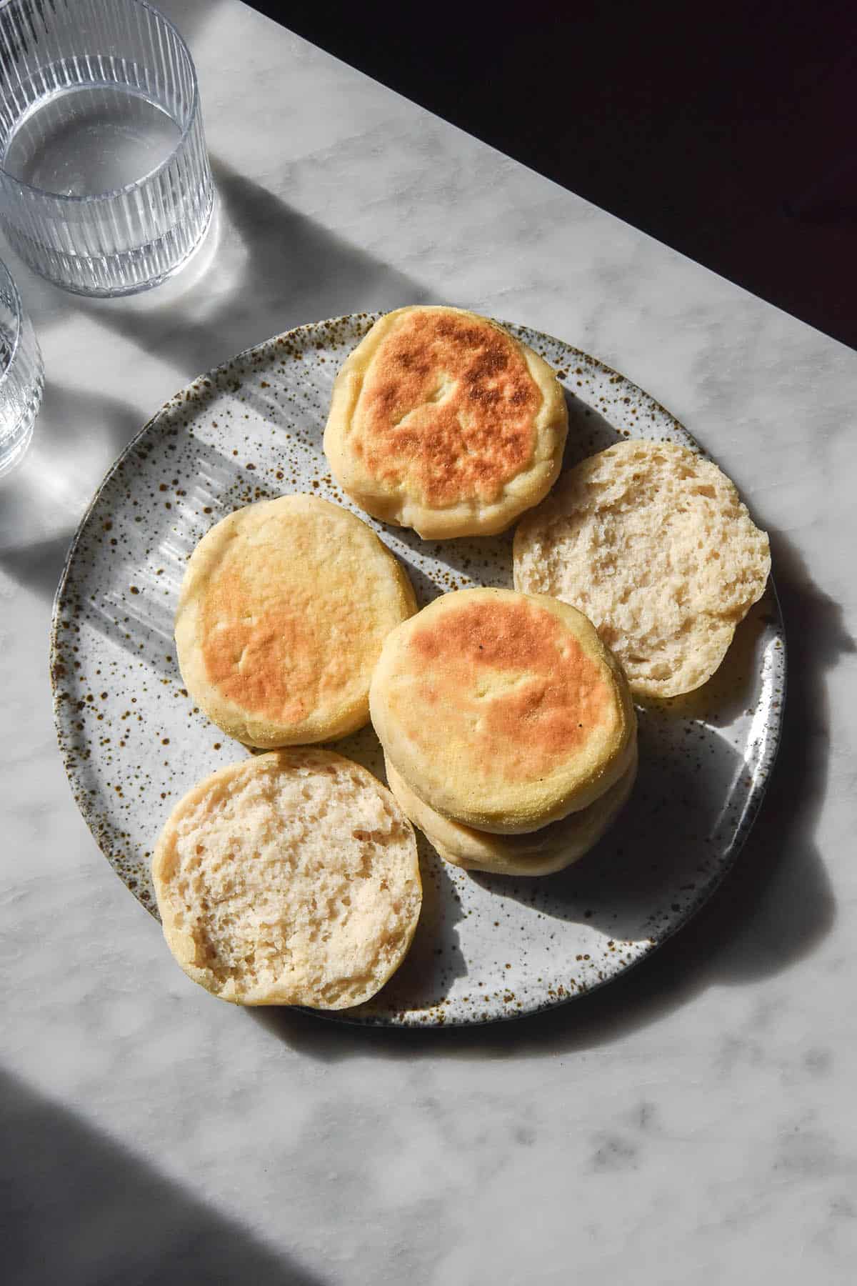 An aerial image of gluten free sourdough English muffins on a white marble table in contrasting sunlight