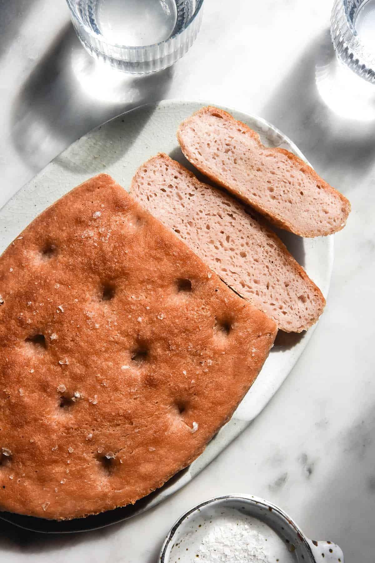 A brightly lit aerial image of a gluten free sourdough focaccia on a white marble table