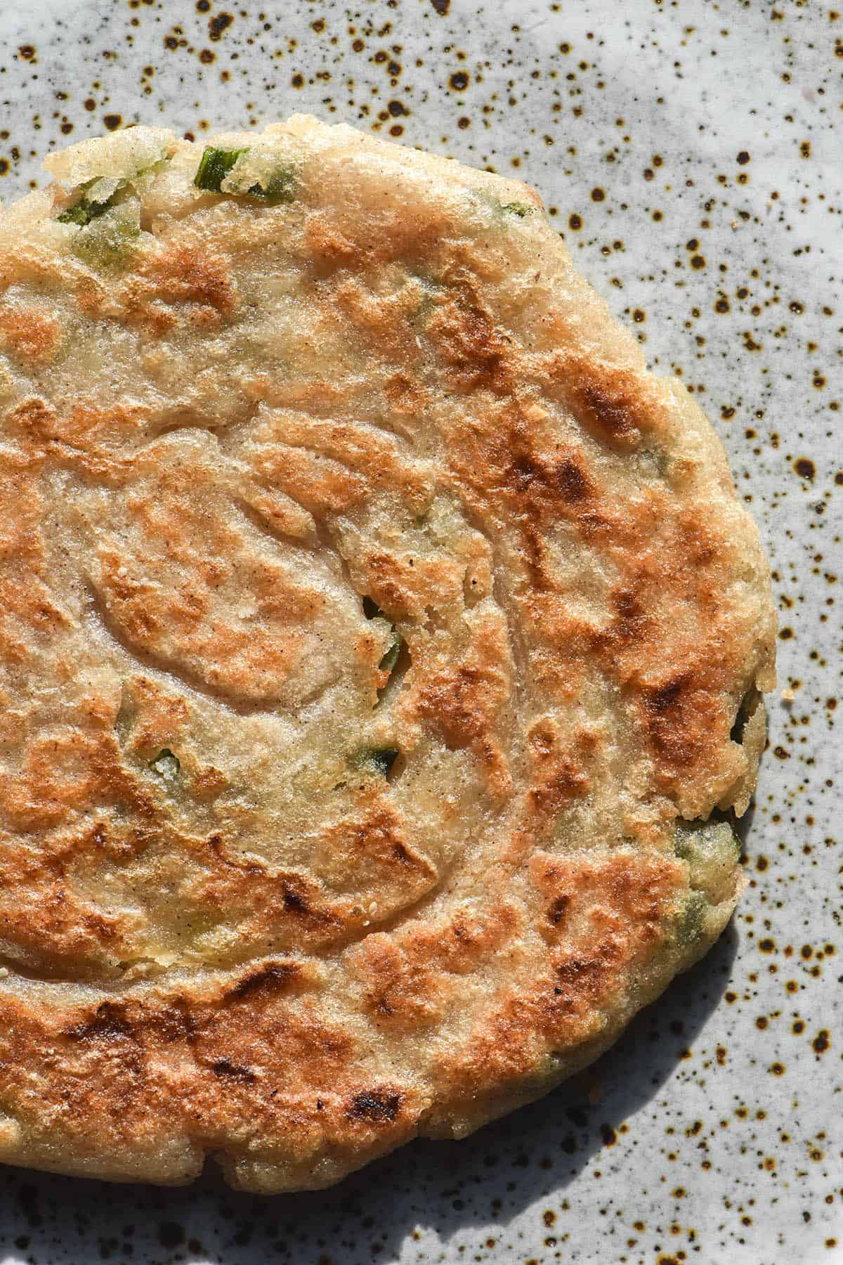 A brightly lit aerial image of a gluten free sourdough discard scallion pancake on a white speckled ceramic plate